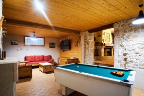 A pool table in a room with wooden ceiling, a red sofa, and stone walls. - Holiday Accommodation "Maison de pierre" with beautiful view (Saint-Gervais)