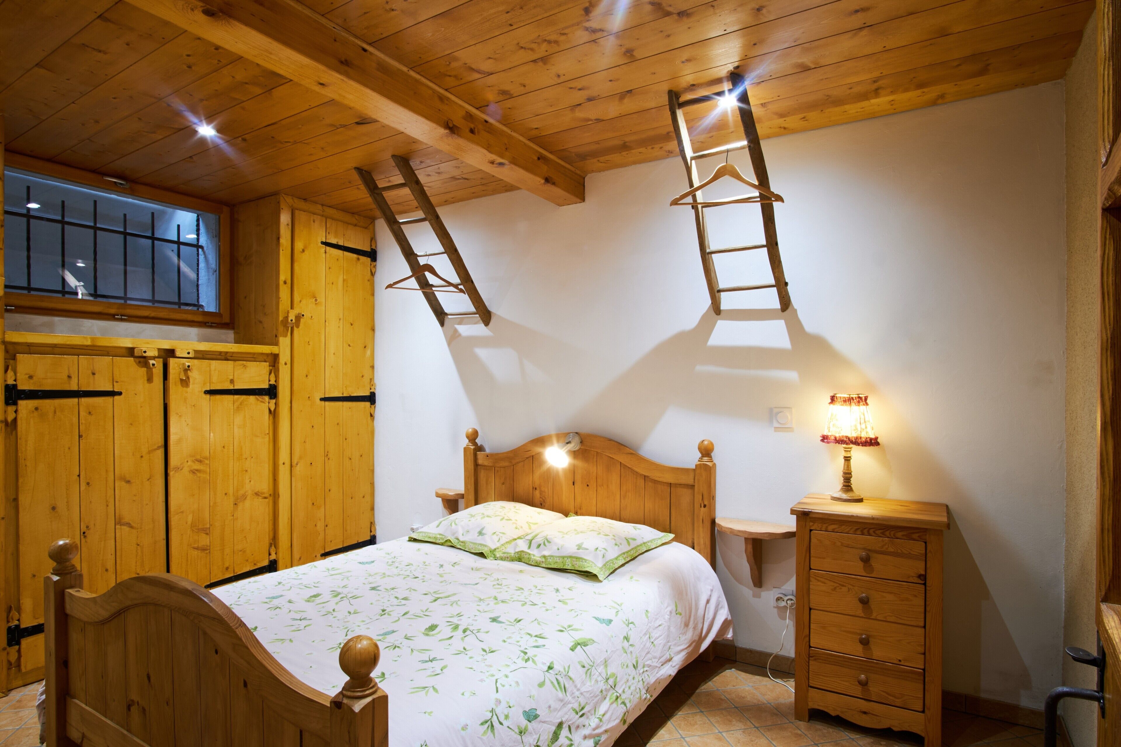 Ein Schlafzimmer aus Holz mit einem Bett, einem Nachttisch, einer Lampe und einem Fenster mit Jalousien.
