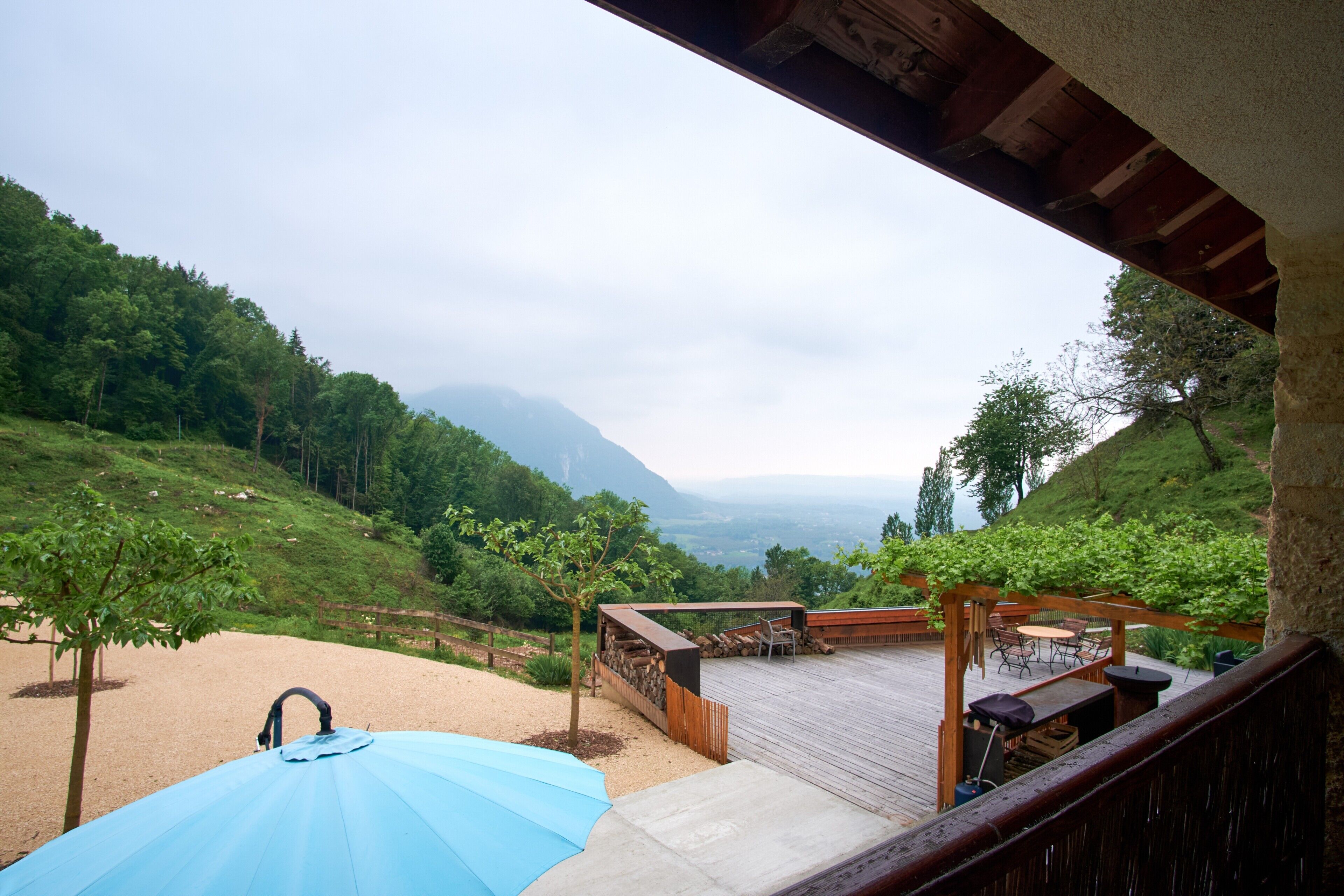 Un terrazzo in legno con mobili da esterno, una pergola e vista su un paesaggio collinare.