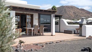 A modern outdoor patio with a table and chairs, a covered seating area, and a mountain backdrop. - Villa "Montaña Roja" with Private Pool, Terraces, and Wi-Fi (Playa Blanca)