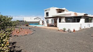 A modern house with a pool, surrounded by a gravel driveway and sparse vegetation. - Villa "Montaña Roja" with Private Pool, Terraces, and Wi-Fi (Playa Blanca)