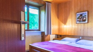 Een kamer met houten lambrisering, een bed, een raam en een deur met een handgreep.