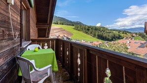 Een balkon met een tafel en stoelen, met uitzicht op een groen landschap met huizen en bomen.