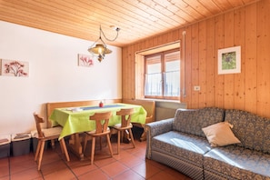 Une pièce aux murs lambrés, comprenant une table à manger, des chaises, un canapé et une fenêtre avec des rideaux.