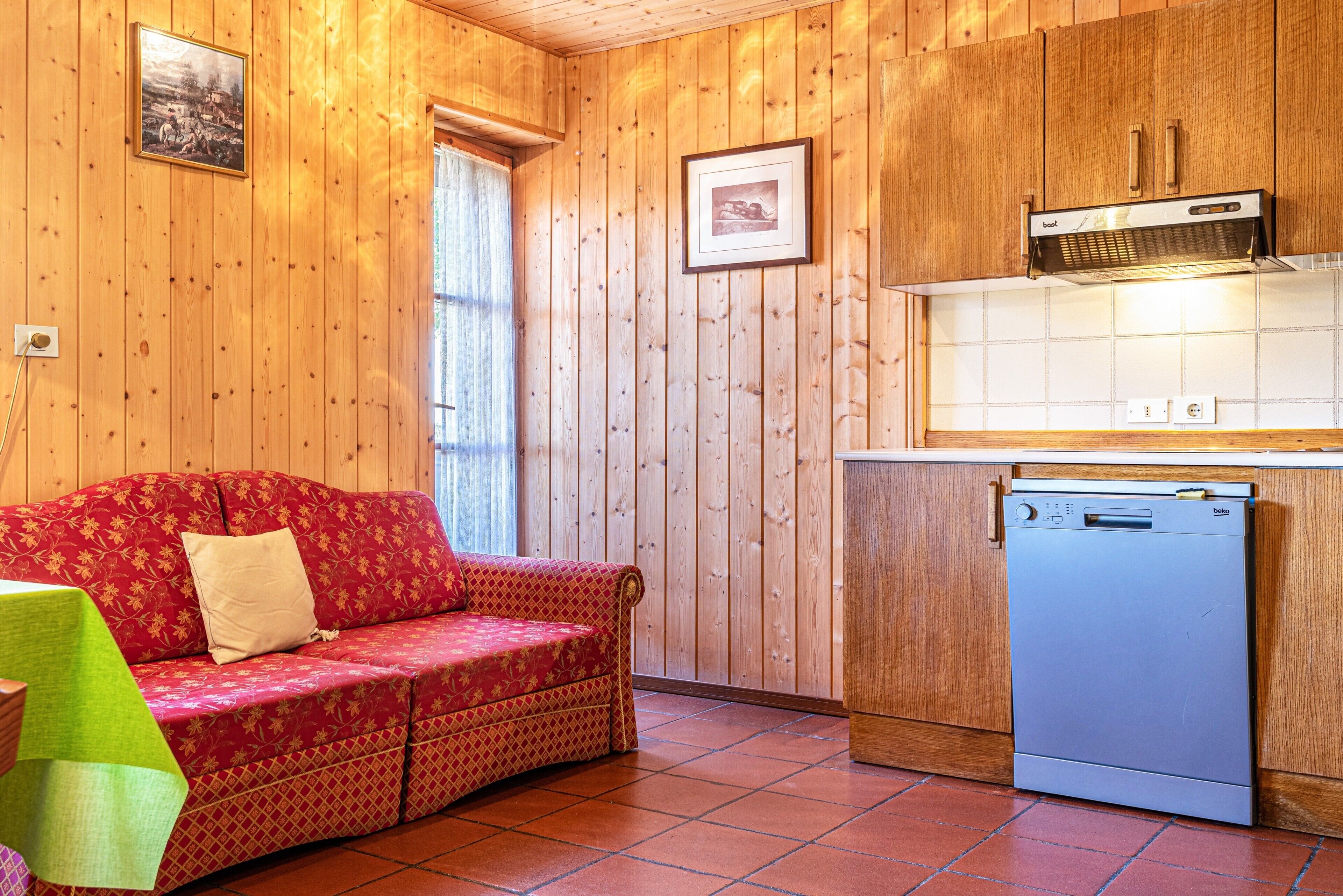 A wooden-paneled room with a sofa, a dishwasher, and a window with curtains.