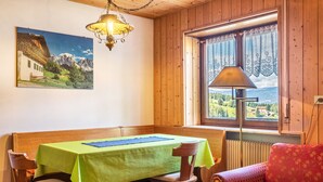 A dining area with a table, chairs, a bench, a sofa, a lamp, a window with curtains, and a painting on the wall.