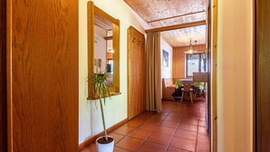 A hallway with wooden walls, a potted plant, a mirror, and a dining area in the background.