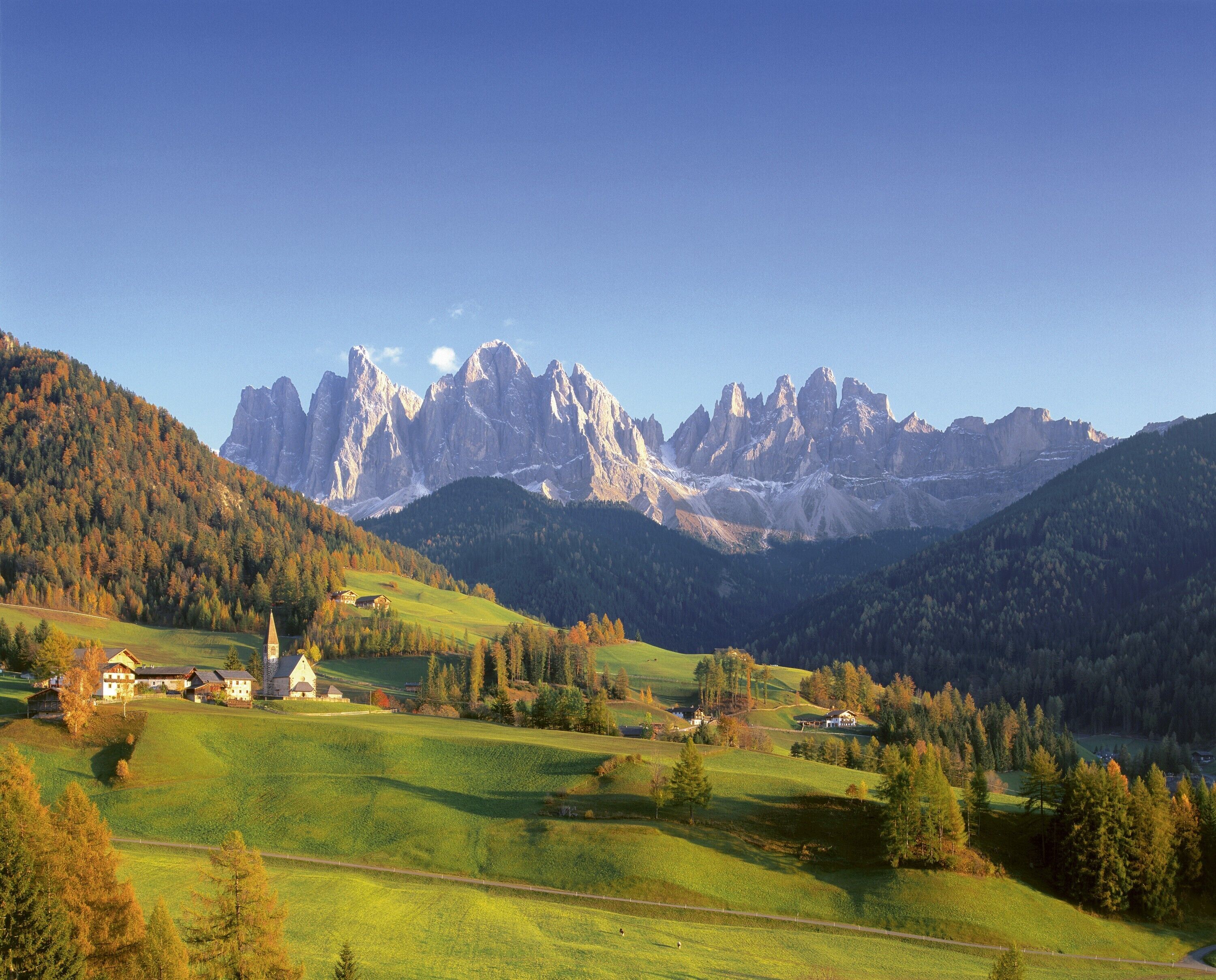 A mountainous landscape with a church, houses, and a clear sky.