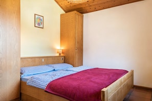A single bed with a wooden headboard, a wooden wardrobe, and a wall-mounted light fixture.