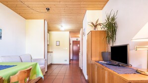 A hotel room with a wooden ceiling, a TV on a wooden stand, a dining table with a green tablecloth, and a sofa. - 'Pension Sonia Apartment 104' with Mountain View, Garden & Wi-Fi (Funes)