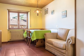 A dining area with a table, chairs, a sofa, a radiator, and a window with a view of a building.