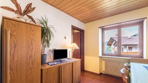 A room with a wooden cabinet, a television, a lamp, a potted plant, and a window with a view of a building. - 'Pension Sonia Apartment 104' with Mountain View, Garden & Wi-Fi (Funes)