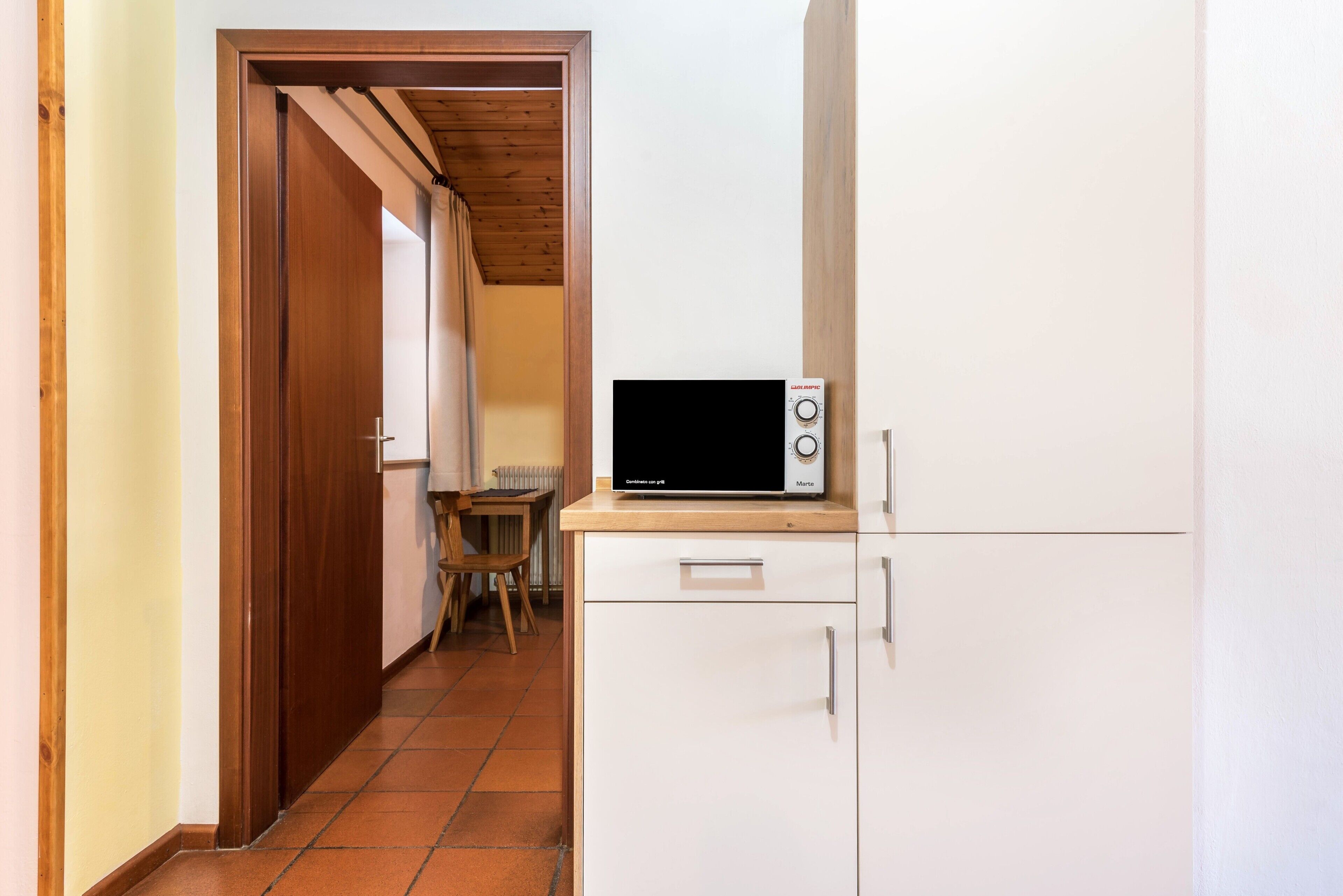 Eine Küche mit einer Mikrowelle auf einem Schrank, einer Holztür und einem gefliesten Boden.