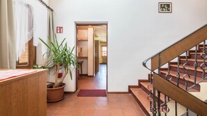 A hallway with a wooden desk, a potted plant, a red mat, a staircase with metal railings, and a door leading to another room. - 'Pension Sonia Apartment 104' with Mountain View, Garden & Wi-Fi (Funes)