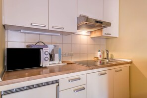 A kitchen with white cabinets, a microwave, a coffee maker, and a sink.