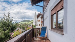 En balkon med en træstol, en hvid parasol og udsigt over et grønt landskab.