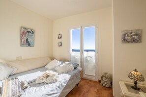 A bedroom with a bed, a nightstand, a lamp, a window with blinds, and a view of the sea. - Holiday Home 'Casa Segerlund' with Sea View, Shared Pool & Wi-Fi (Almuñécar)