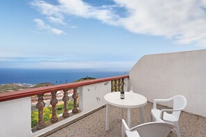 A balcony with a table and chairs, a bottle of wine, and a view of the ocean.