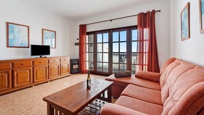 Una sala de estar con un sofá, una mesa de centro de madera, un televisor y un aparador.