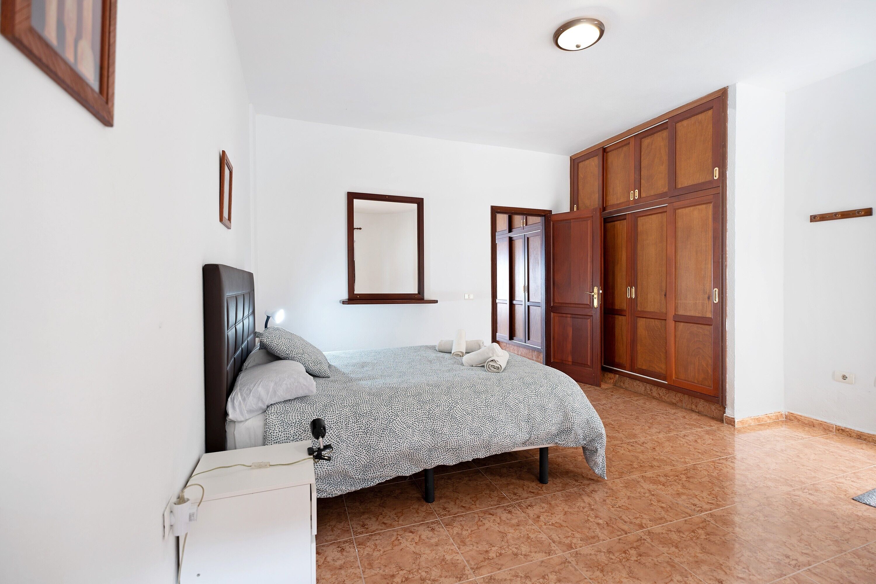A bedroom with a bed, a wardrobe, a mirror, and a bedside table.