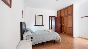 A bedroom with a bed, a wardrobe, a mirror, and a bedside table.