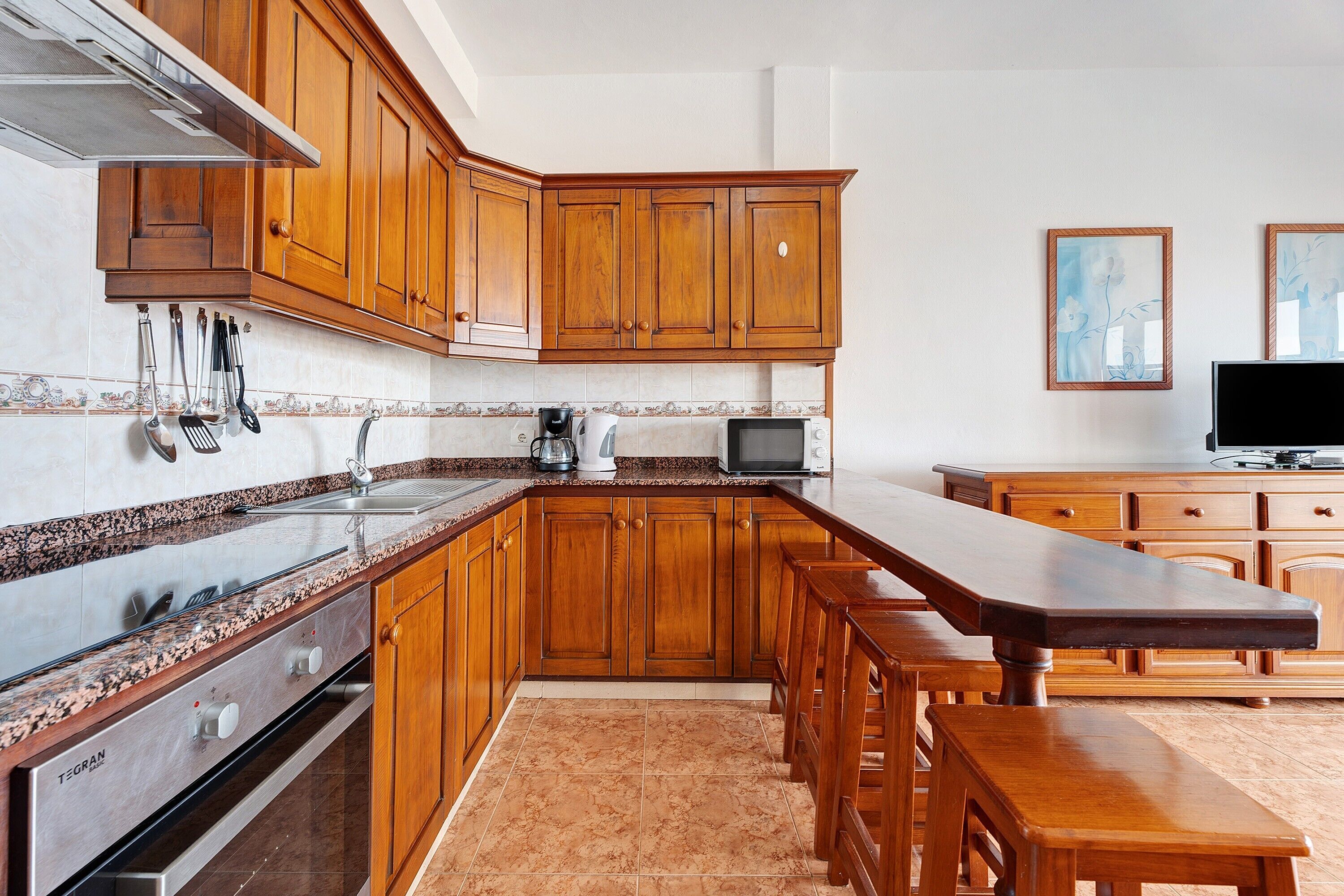 A kitchen with wooden cabinets, a granite countertop, stainless steel appliances, and a wooden dining table with benches.