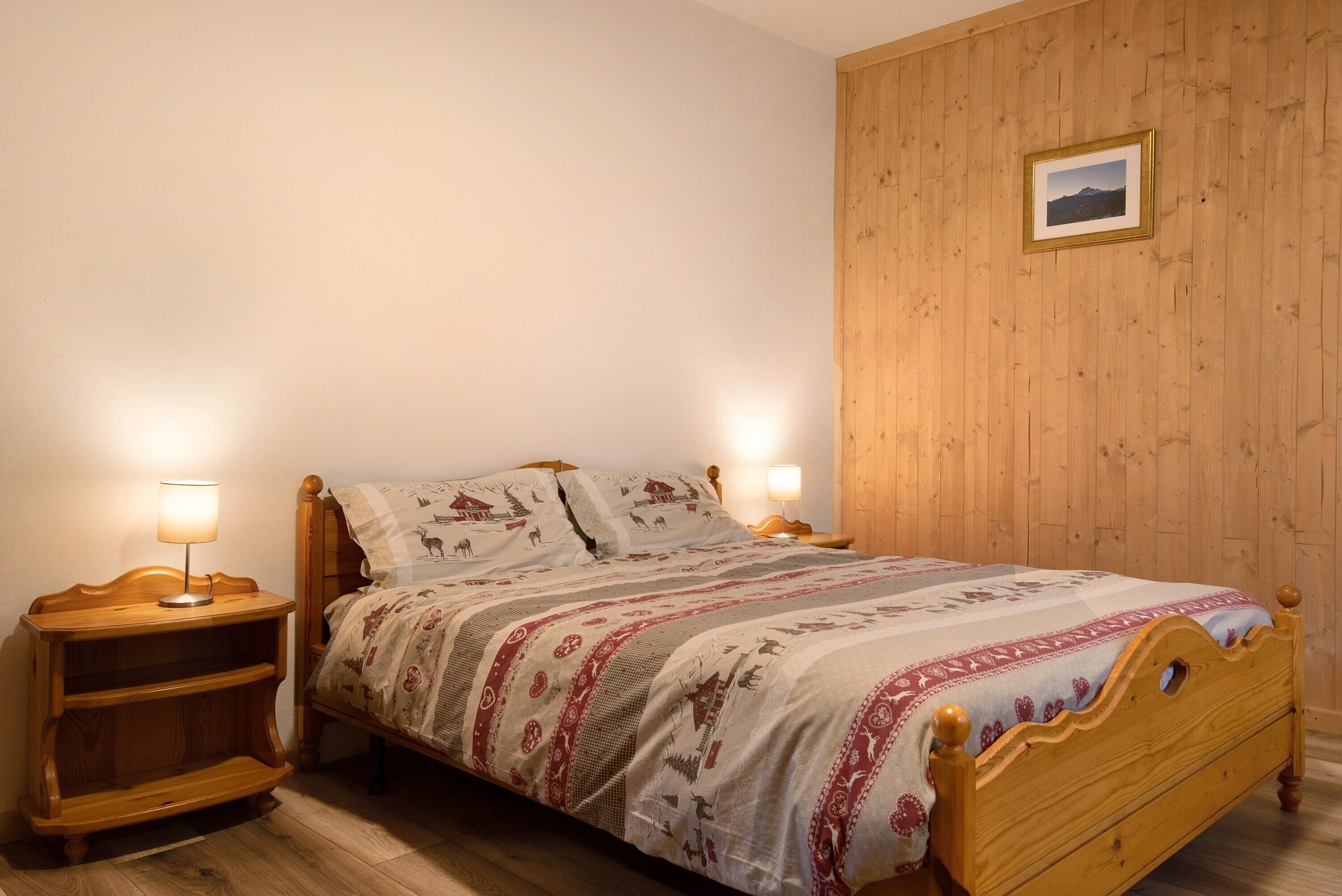 A wooden bed with a patterned bedspread, two bedside tables with lamps, and a framed picture on the wall.