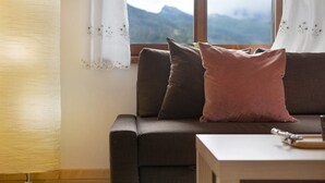 A sofa with two pillows, a table with a knife and a cutting board, and a window with a view of mountains. - Apartment 'Lorenzo' with Mountain View, Balcony and Wi-Fi (Vodo)