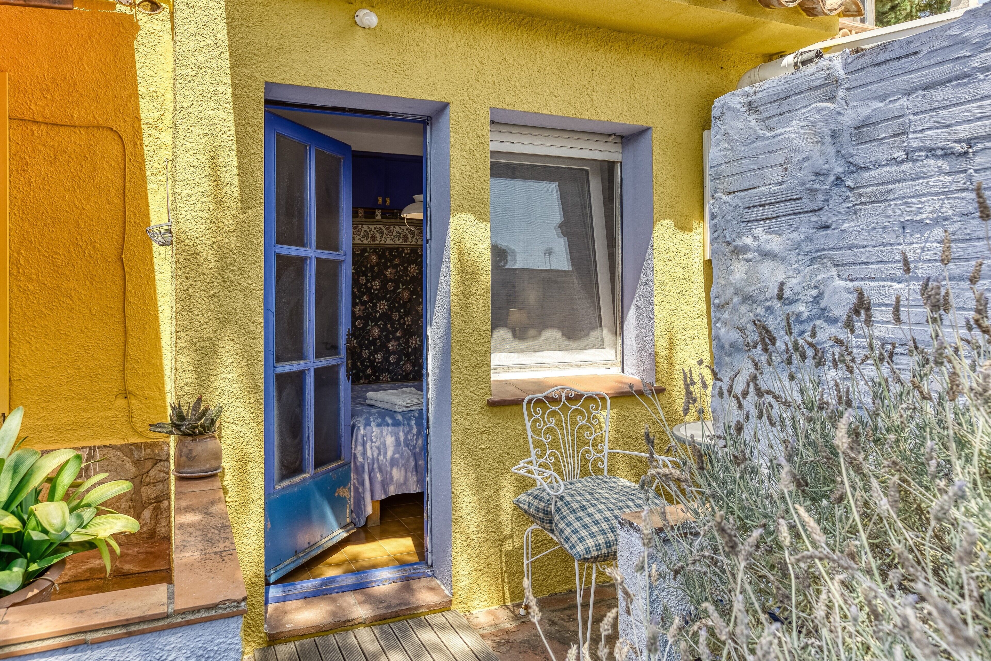 A yellow exterior wall with a blue door and window, a white chair, and a small table.