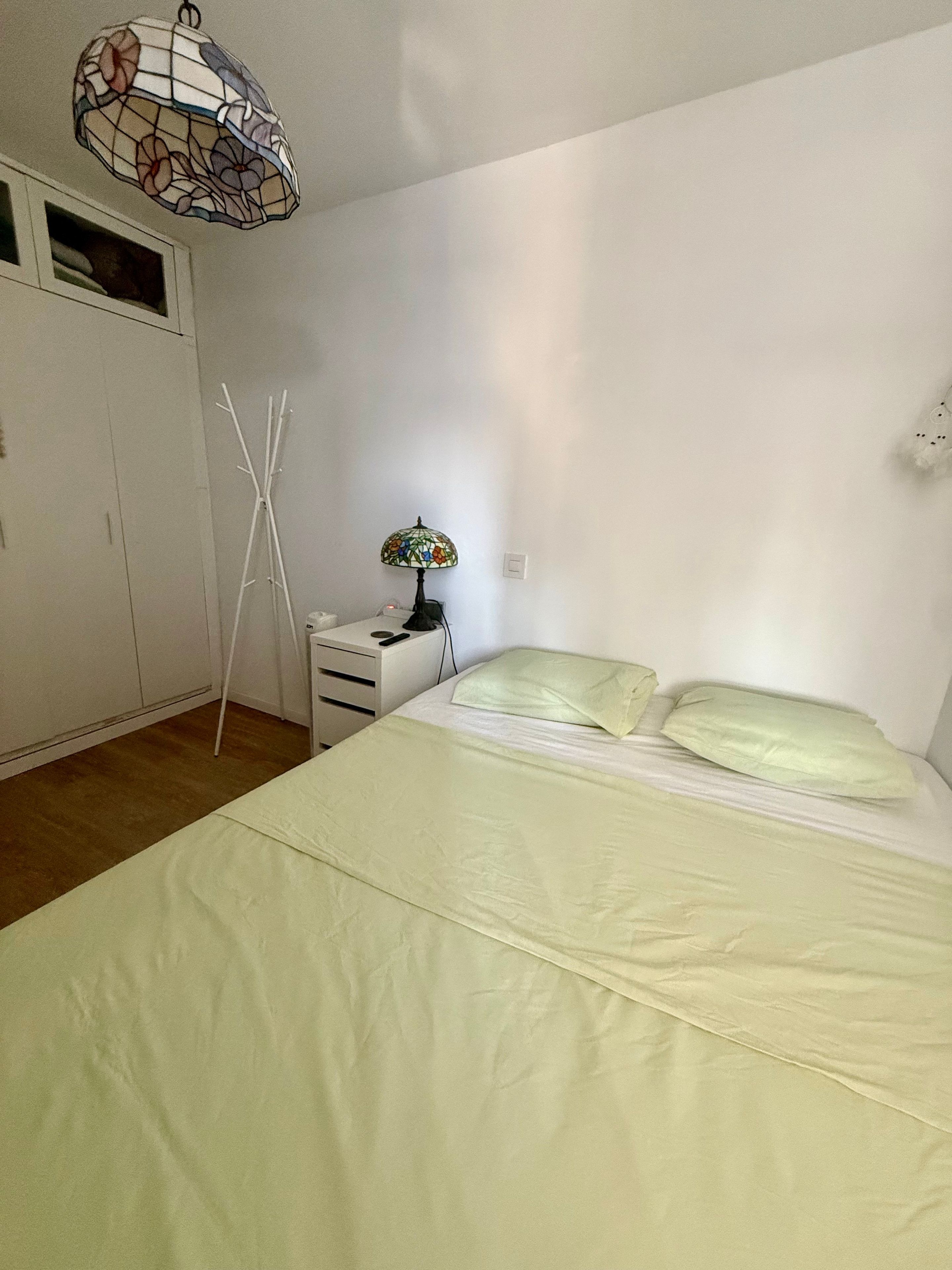 Een slaapkamer met een bed, een nachtkastje, een lamp, een kledingkast en een decoratieve plafondlamp.