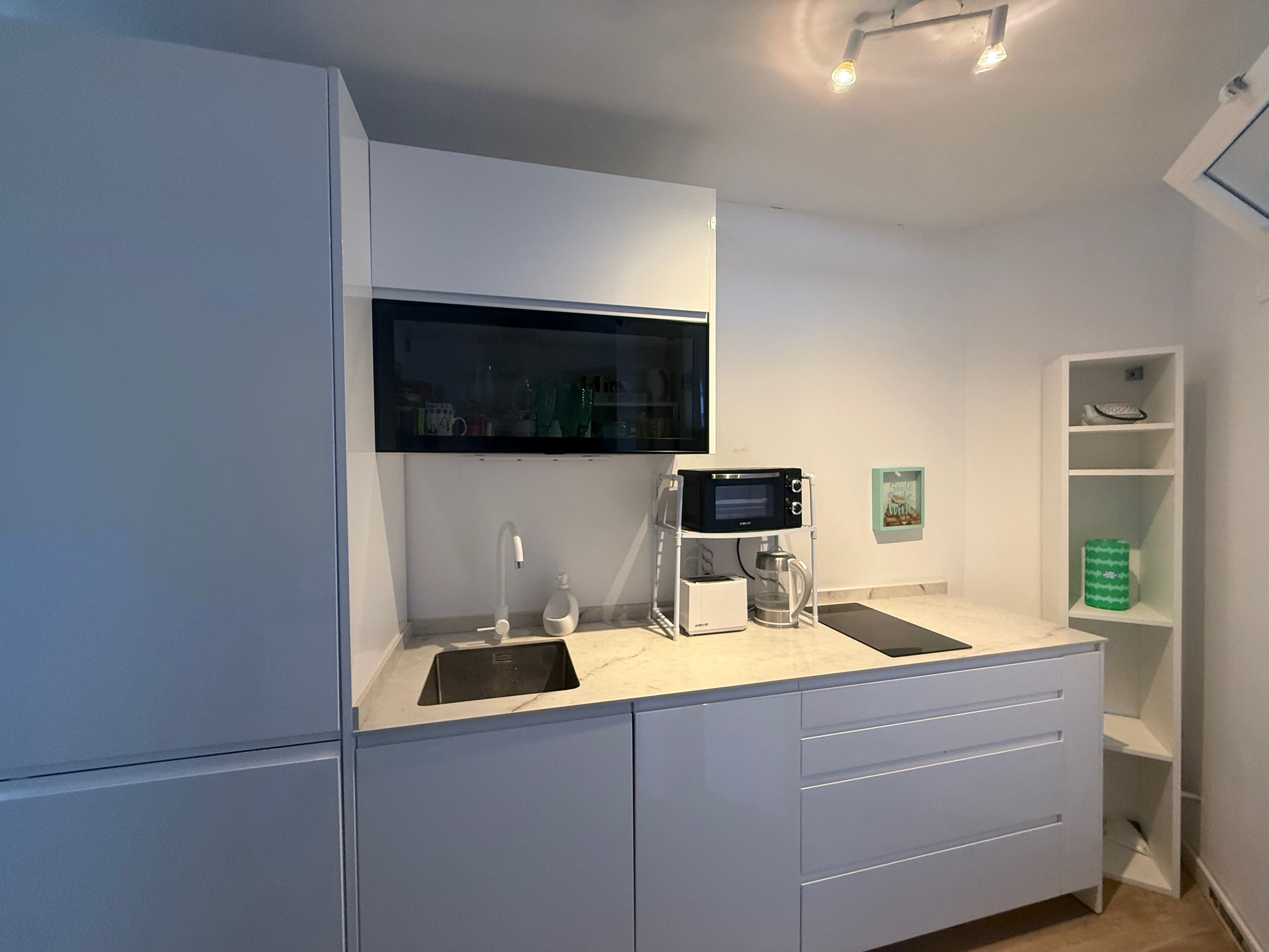 Een moderne keuken met witte kastjes, een ingebouwde magnetron, een koffiezetapparaat en een spoelbak.