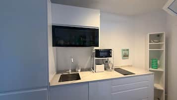 Een moderne keuken met witte kastjes, een ingebouwde magnetron, een koffiezetapparaat en een spoelbak.