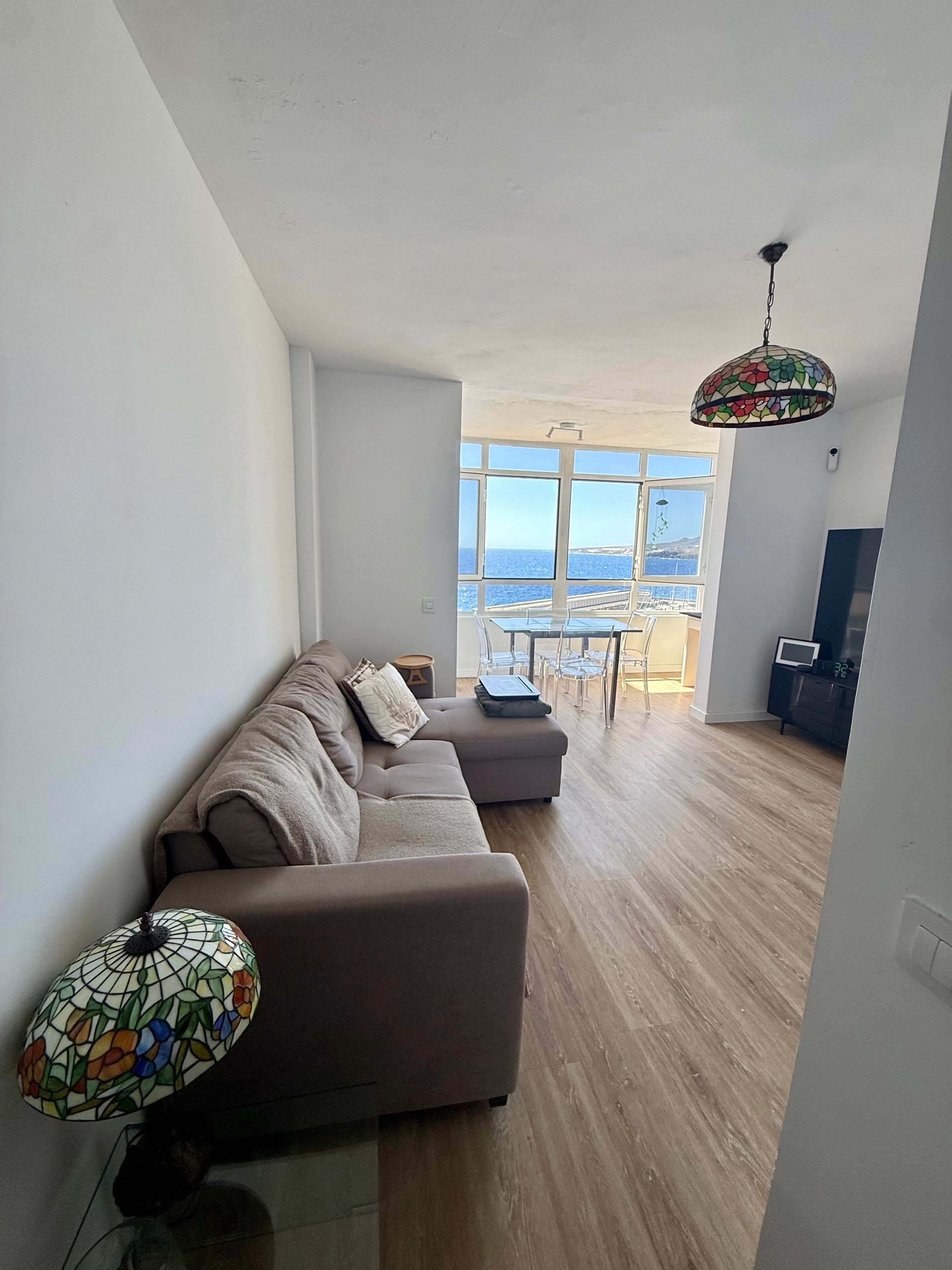 Een moderne woonkamer met een ruime bank, een eethoek met tafel en stoelen, en uitzicht op zee door grote ramen.