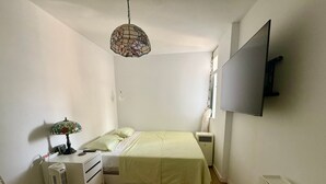 A small, well-lit bedroom with a bed, bedside tables, a lamp, a heater, and a TV mounted on the wall. - Holiday Home 'Sea view Apartment' with Sea View, Shared Pool & Wi-Fi (Candelaria)