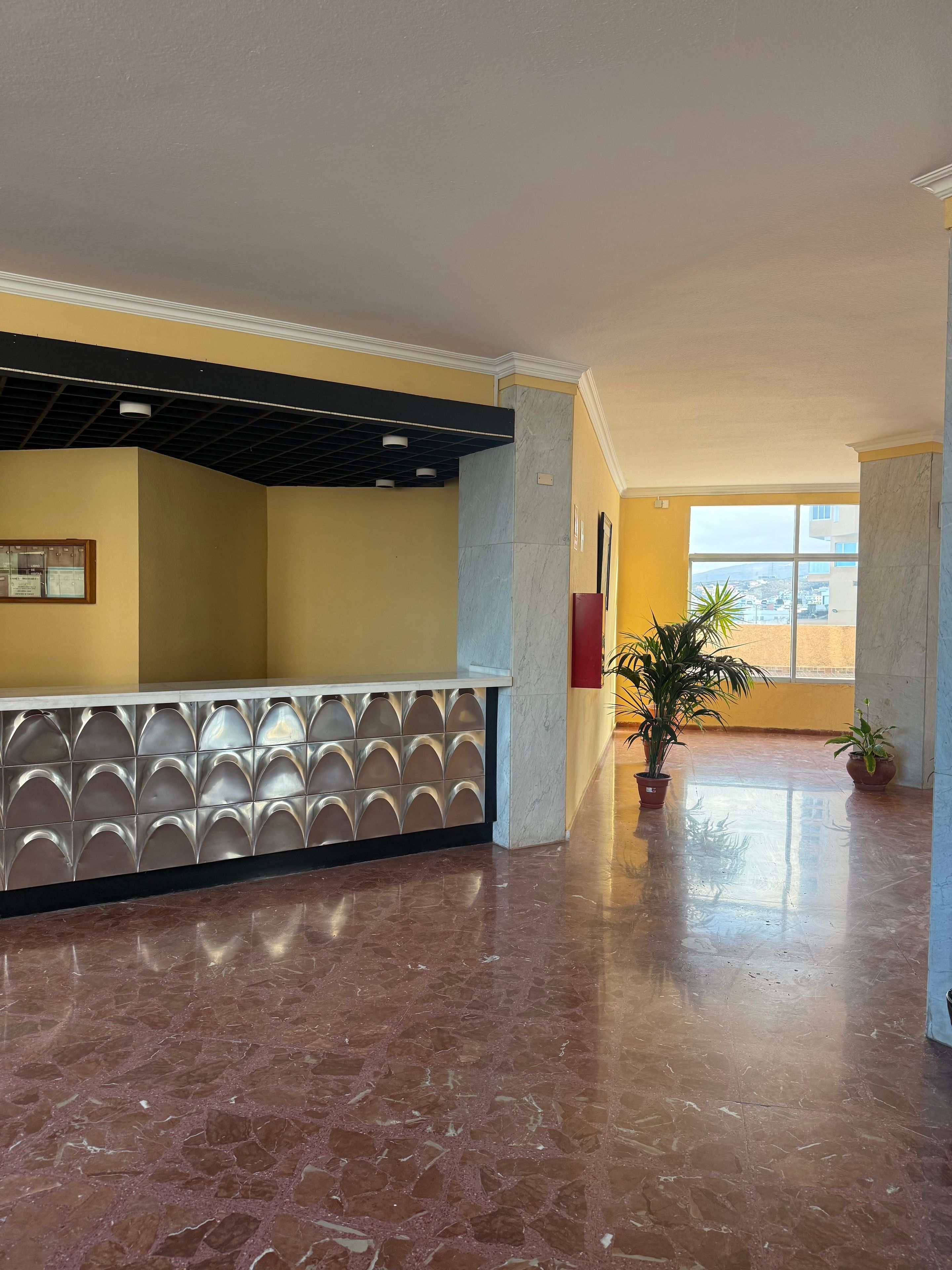 Een ruime lobby met een marmeren vloer, een receptiebalie met een decoratieve achterwand en potplanten.