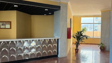 Een ruime lobby met een marmeren vloer, een receptiebalie met een decoratieve achterwand en potplanten.