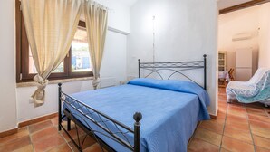 Un dormitorio con cama, cortinas, una ventana y una puerta que da a otra habitación.