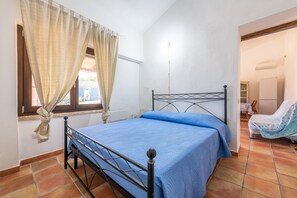 A bedroom with a bed, curtains, a window, and a door leading to another room.