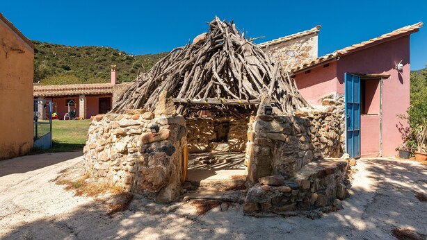 Una construcción de piedra con techo de paja, pared de piedra y puerta de madera.