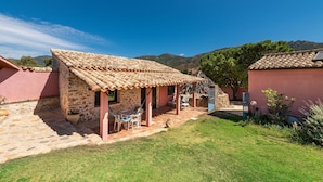 Un edificio de piedra con techo de tejas, un patio cubierto con sillas y un patio con césped.