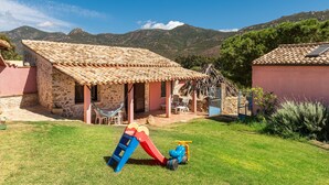 Una casa de piedra con techo de tejas, un patio con mobiliario exterior y un parque infantil.