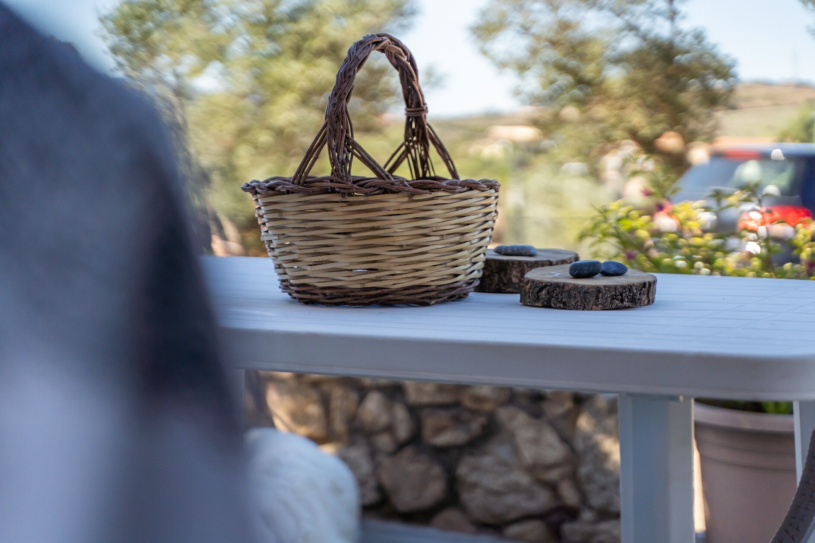 A wicker basket on a white table with a stone wall and greenery in the background.