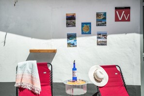 A room with two red lounge chairs, a small table with a bottle, a hat, and wall art.