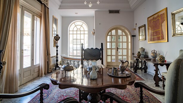 Um quarto com uma grande mesa de madeira, cadeiras ornamentadas, um lustre e decoração clássica.