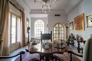 Une pièce dotée d’une grande table en bois, de fauteuils richement décorés, d’un lustre et d’un décor classique.