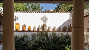 Um pátio com parede de azulejos, diversos vasos de cerâmica e um pequeno jardim com flores amarelas.