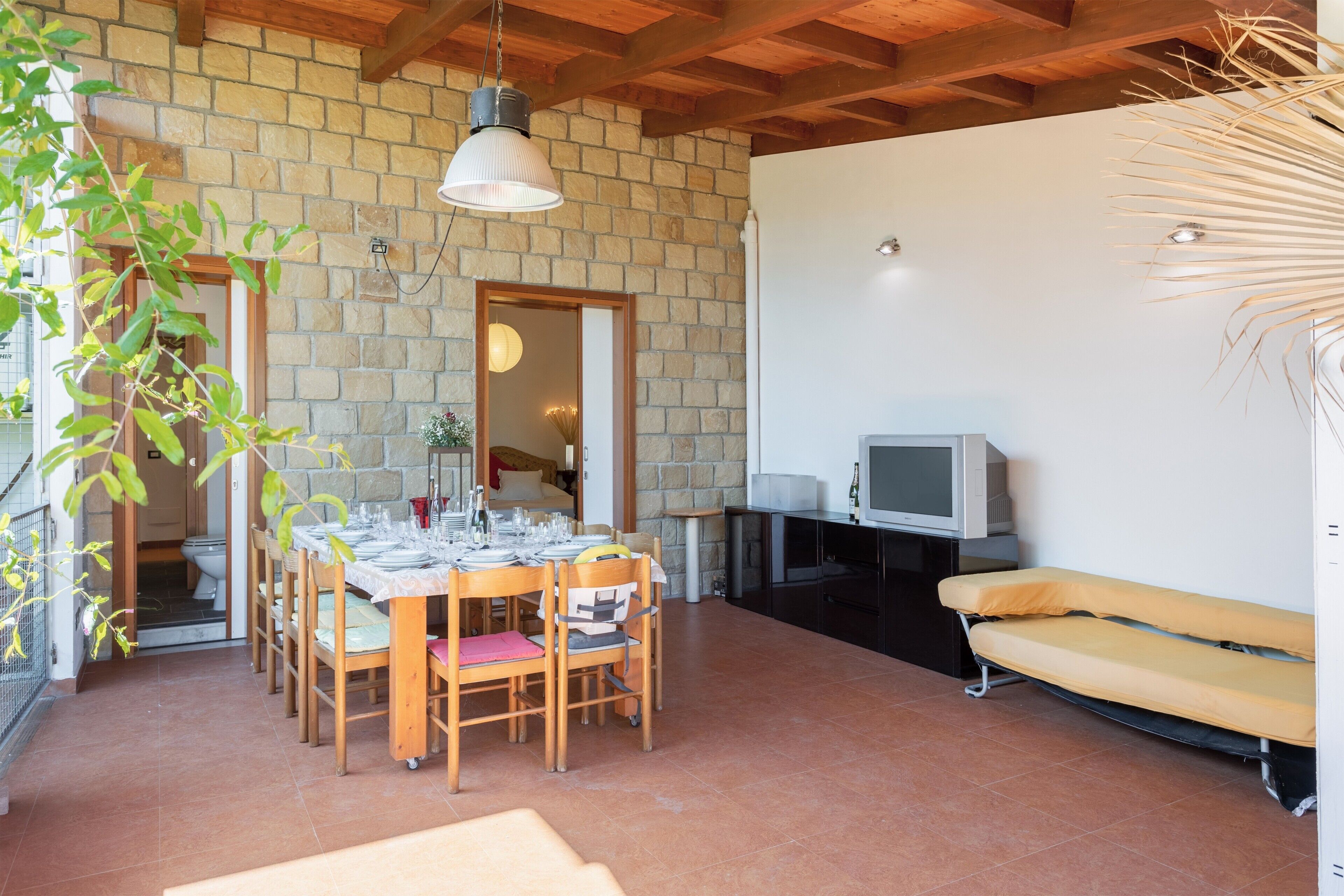 A dining area with a brick wall, wooden ceiling, and a TV on a stand.