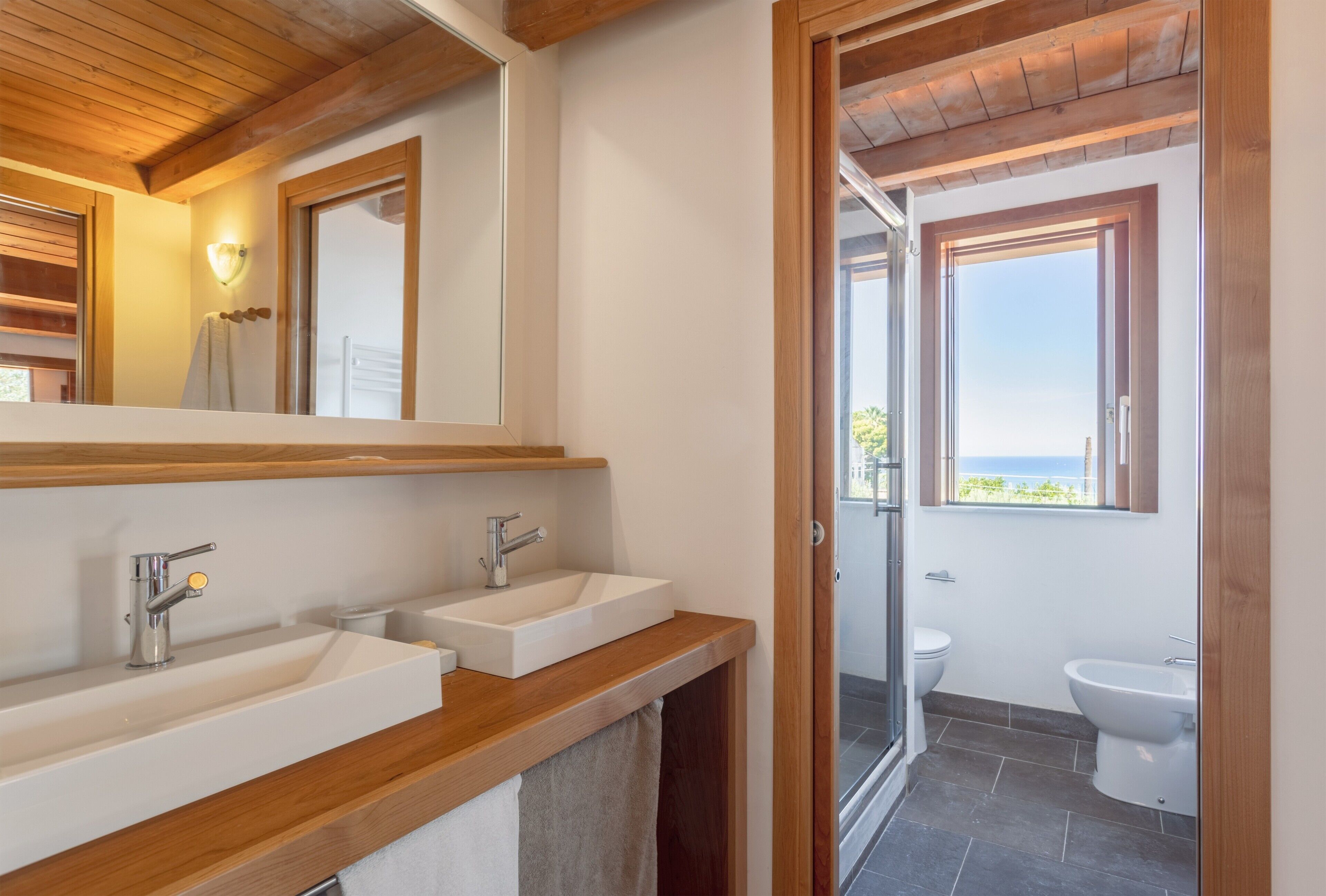 A bathroom with two sinks, a mirror, and a view of the sea through a window.