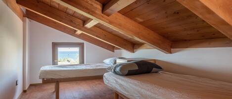 Quarto com duas camas de solteiro, vigas de madeira, uma janela e vista para o exterior.