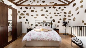 Ein Schlafzimmer mit Steinwand, Holzbalkendecke, einem Bett mit floralem Bettzeug, Nachttischen und einer Stehlampe.